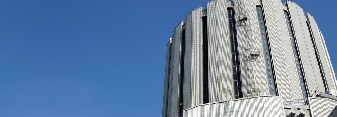 Upper exterior of a large industrial energy facility building with vertical metal cladding against a clear blue sky