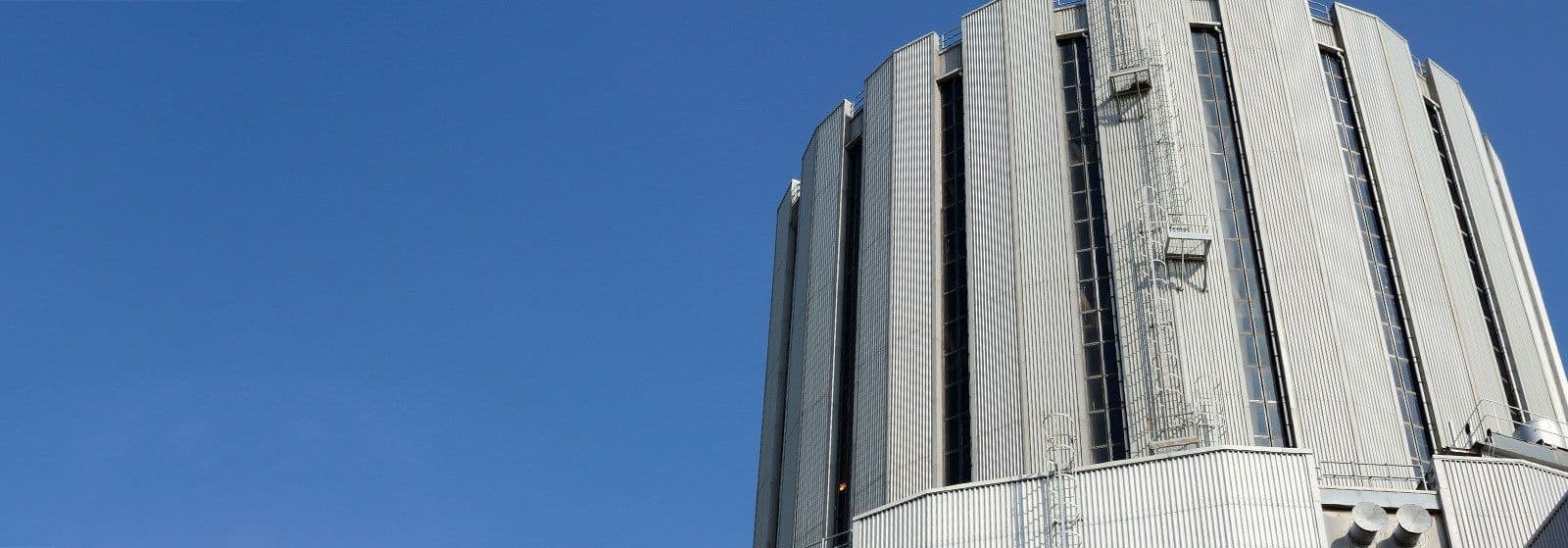 Upper exterior of a large industrial energy facility building with vertical metal cladding against a clear blue sky