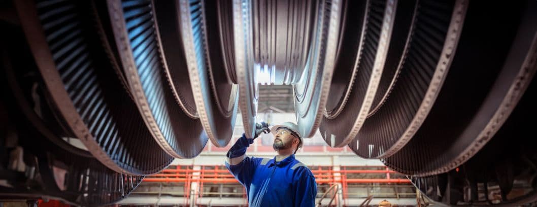 A person in a hard hat looking at industrial equipment in a work facility.