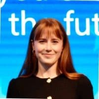Woman in black button up cardigan smiles at the camera infront of a blue background