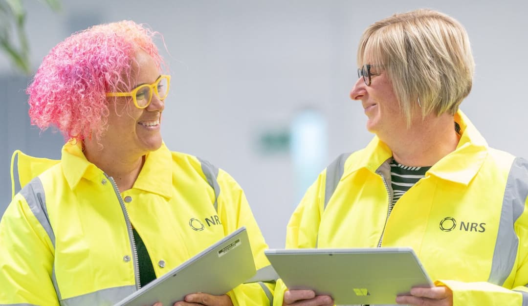 Two women in high vis jackets holding laptops Two women in high vis jackets holding laptops