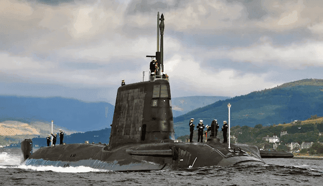 Royal Navy submarine underway with crew visible on the deck and hills in the background
