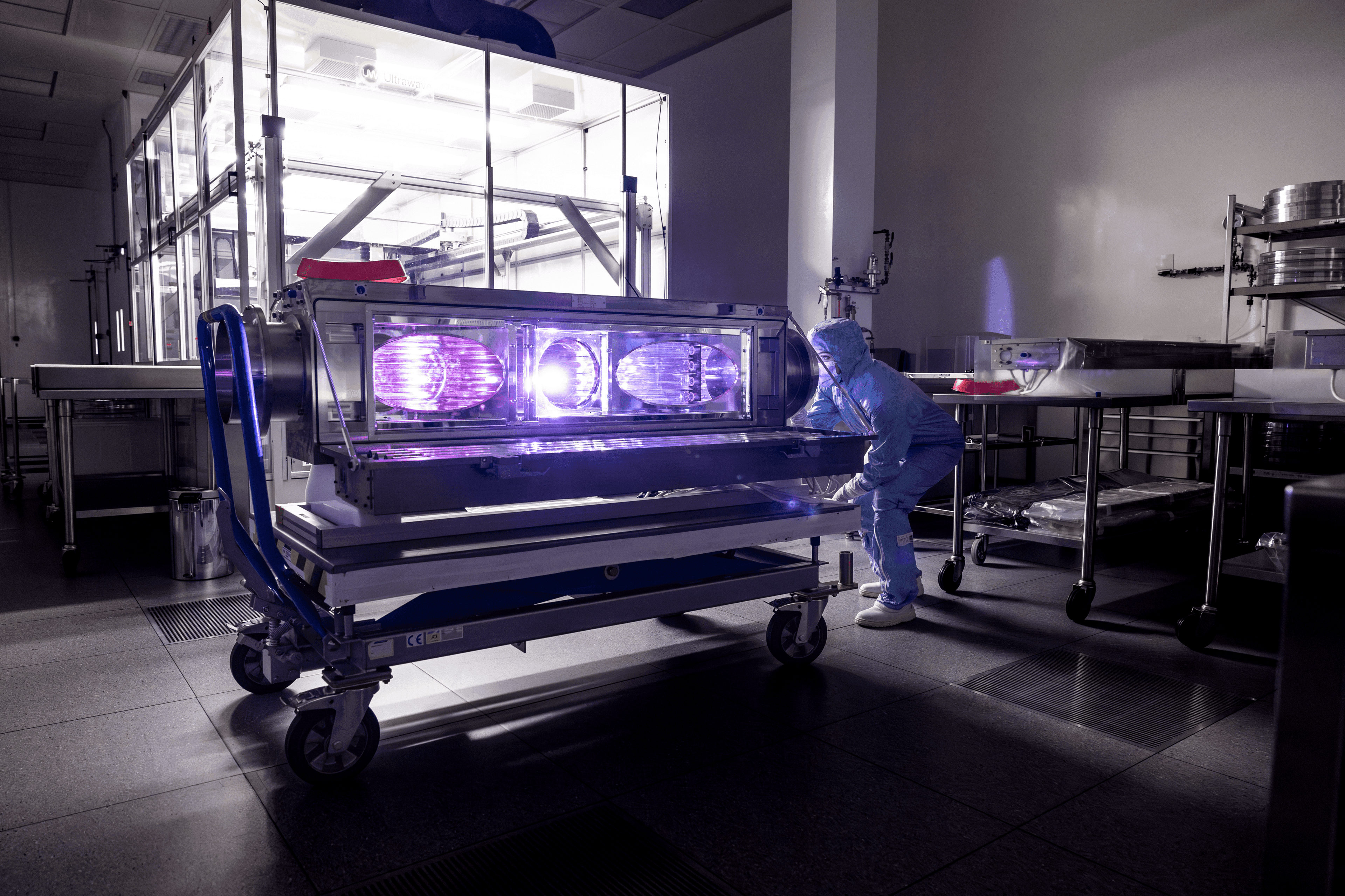 Cleanroom technician moving a large equipment unit with bright inspection lamps