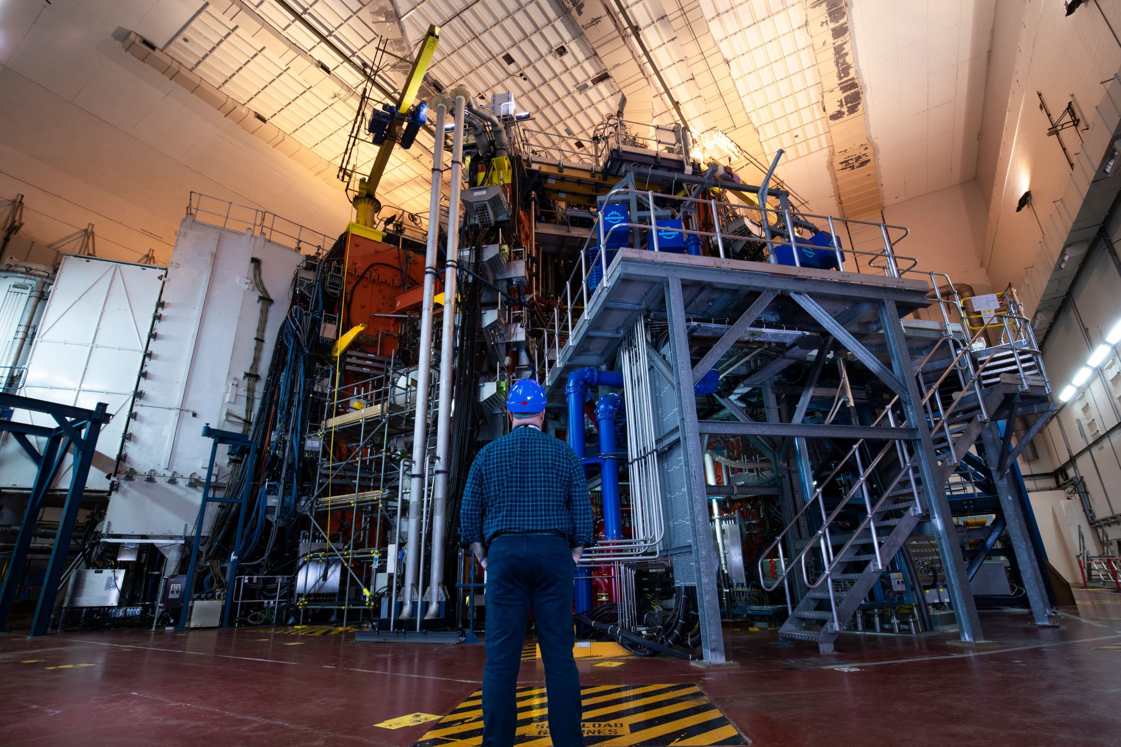 Engineer in a hard hat looking at large industrial equipment inside a high-bay facility