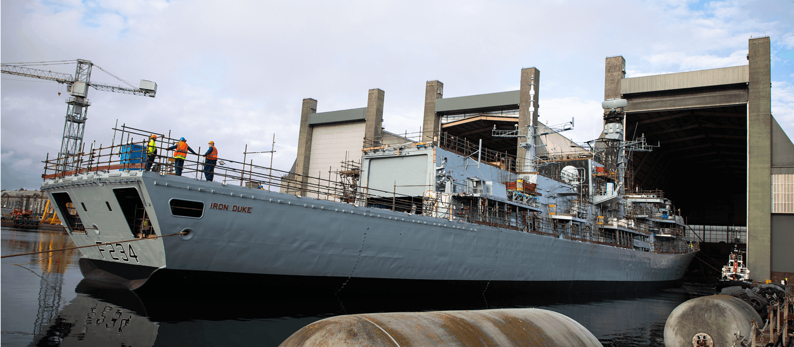 A military-style grey warship sailing through open water with waves breaking at the bow.
