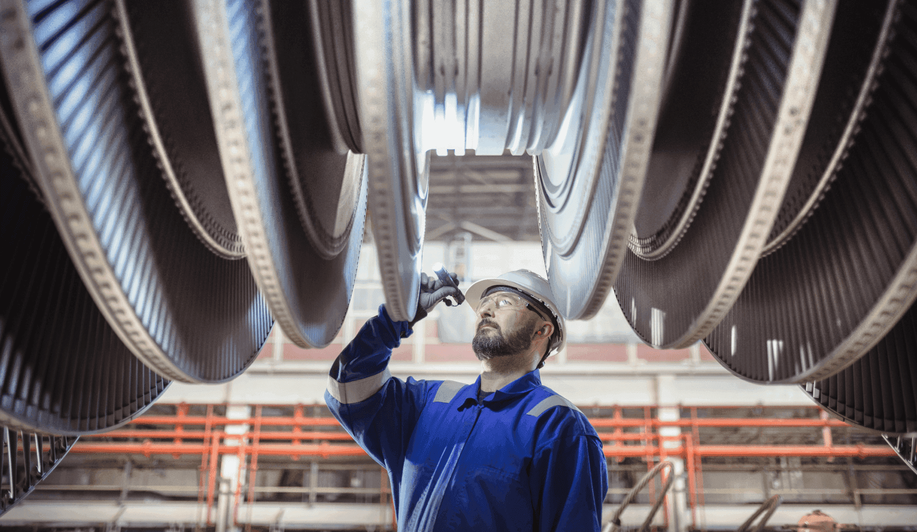 Worker in a hard hat and safety glasses inspecting large industrial turbine blades.