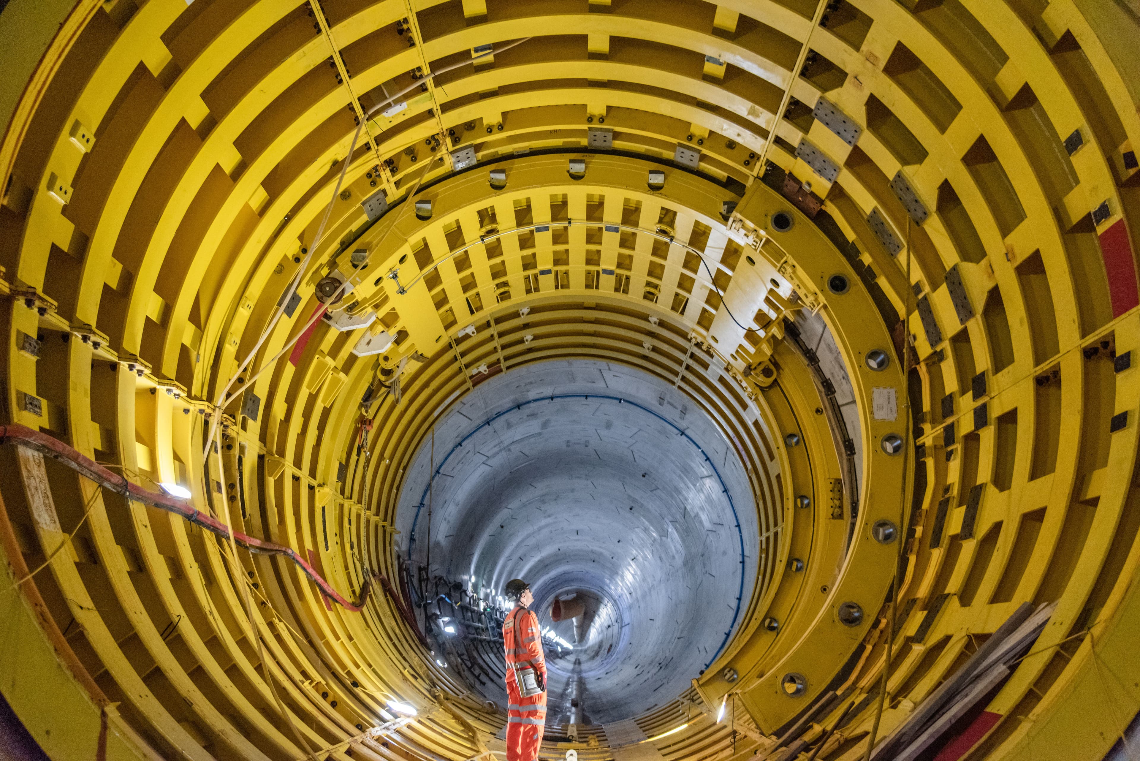 Worker in high-visibility PPE standing inside a large cylindrical industrial structure (tunnel-like interior)